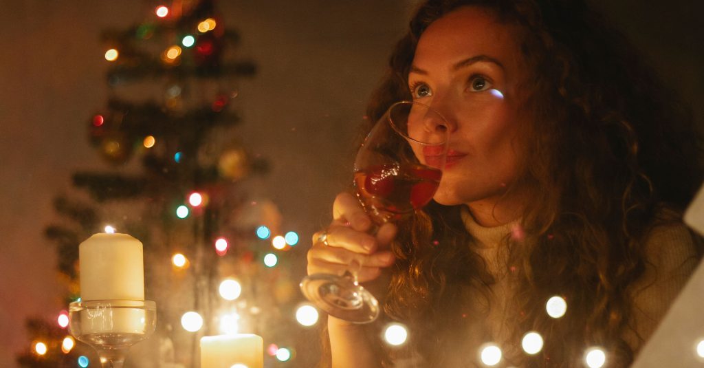 Best Wines for Holiday Hosting: Your 2026 Guide Through glass of dreamy female with glass of champagne sitting among shiny garlands and burning candles during Christmas celebration