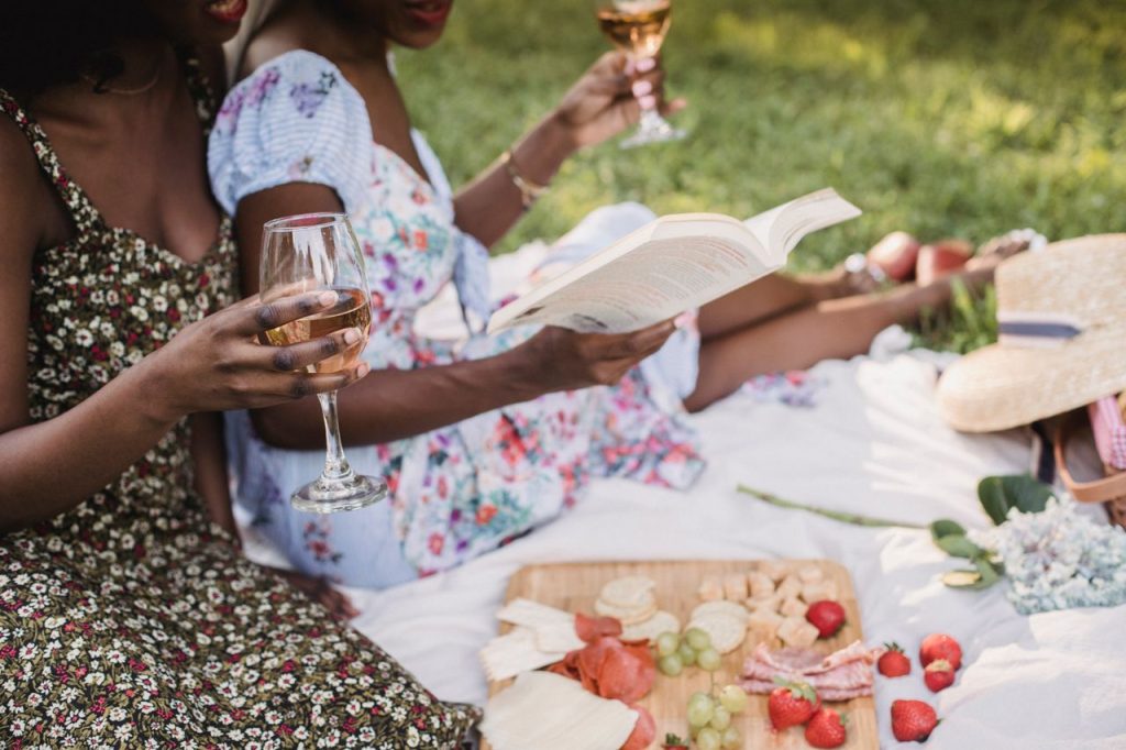 Top Wine Books for Beginners: Best Picks for 2026 Two women sharing a relaxing summer picnic with wine and a book outdoors in a park.